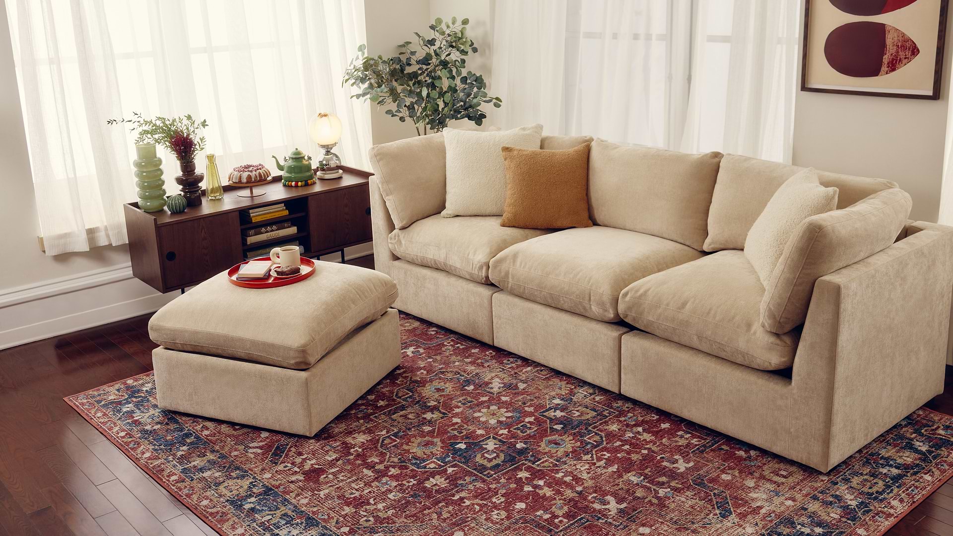 Large beige sectional with ottoman and red traditional rug.